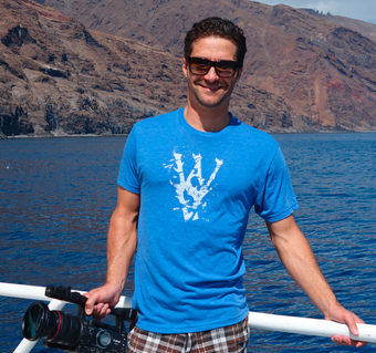 Skyler Thomas wearing baby-blue tri-blend shirt in Isla de Guadalupe. WSV logo on front. Sharks don't kill people, I kill people on back.